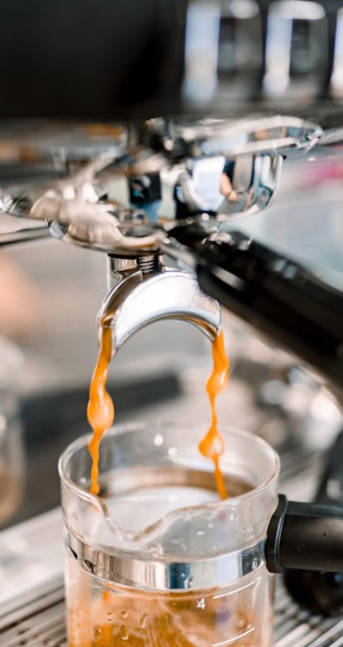 Close-up of espresso machine pouring coffee into a glass, with rich brown liquid flowing down.